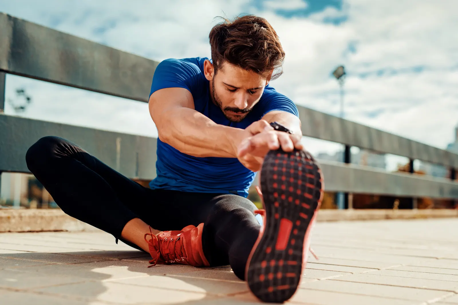 Man in blue athletic wear stretching his leg outdoors before a run as part of athletic recovery