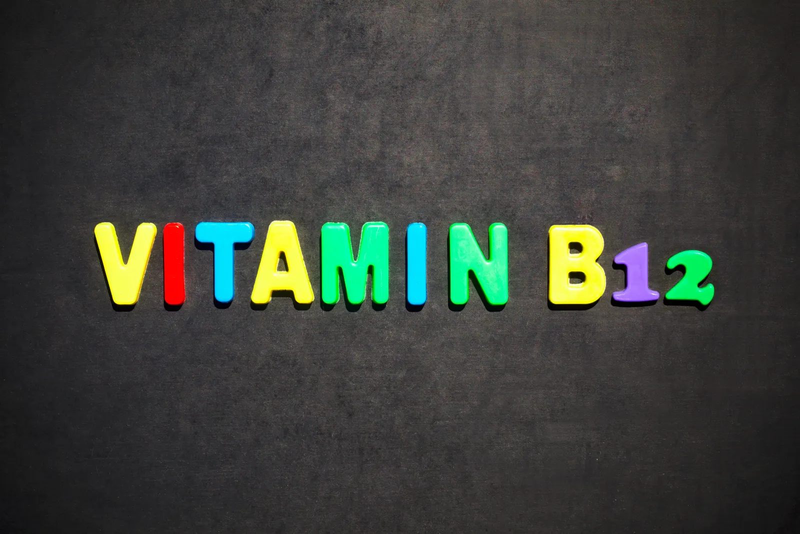 Colorful magnetic letters spelling Vitamin B12 on a dark slate background