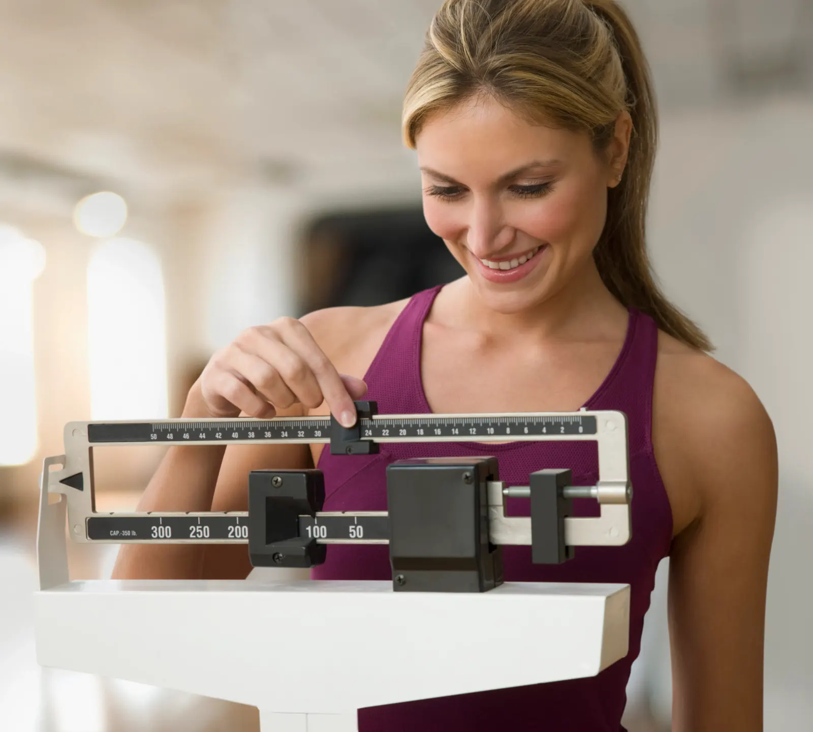 Smiling woman adjusting a balance-beam scale during a weight loss check at a New Rochelle clinic