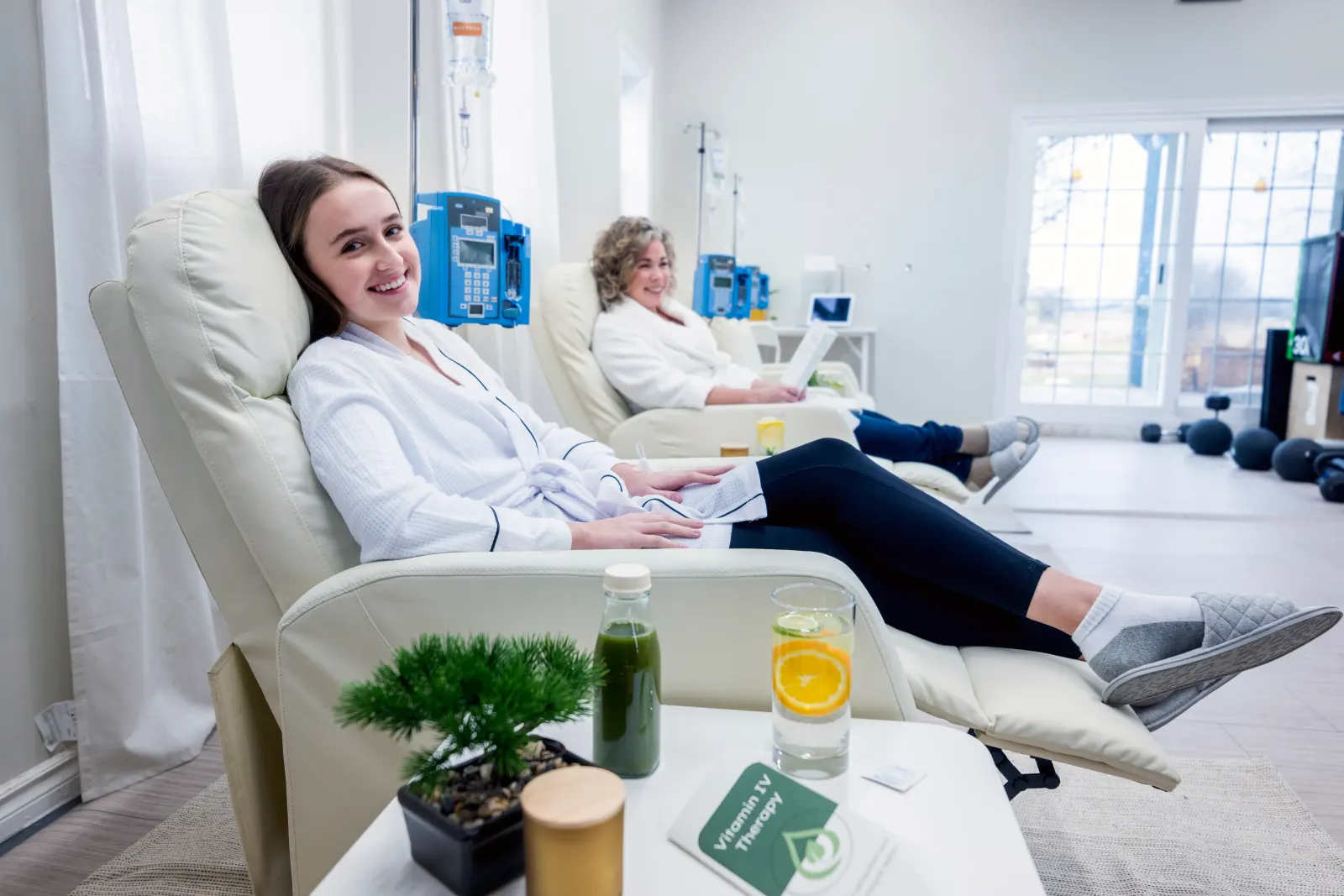 Two women relaxing in recliners during vitamin IV therapy with green juice and citrus water at a New Rochelle clinic