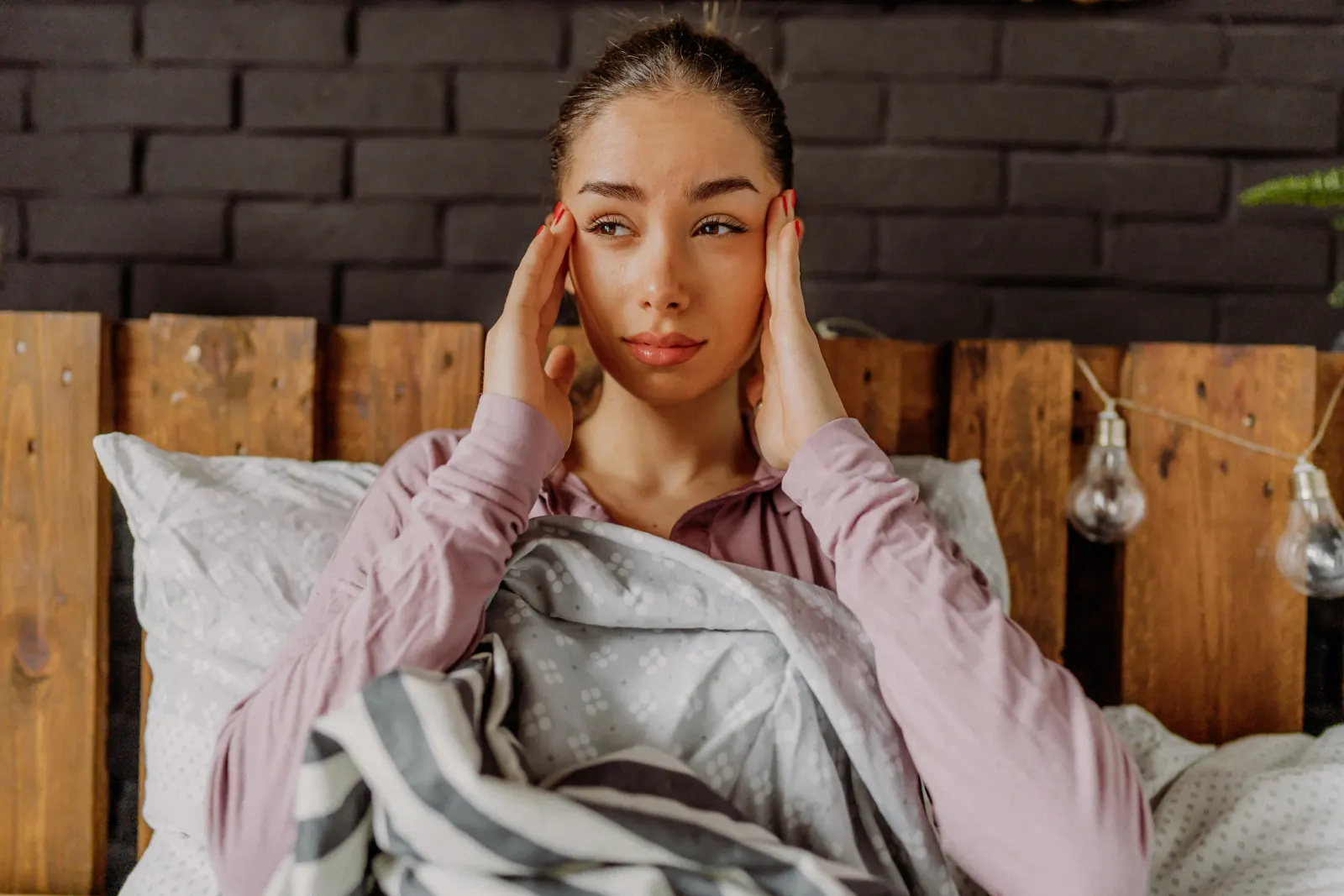 Woman in bed rubbing her temples with a morning headache, a sign hangover recovery IV therapy can ease