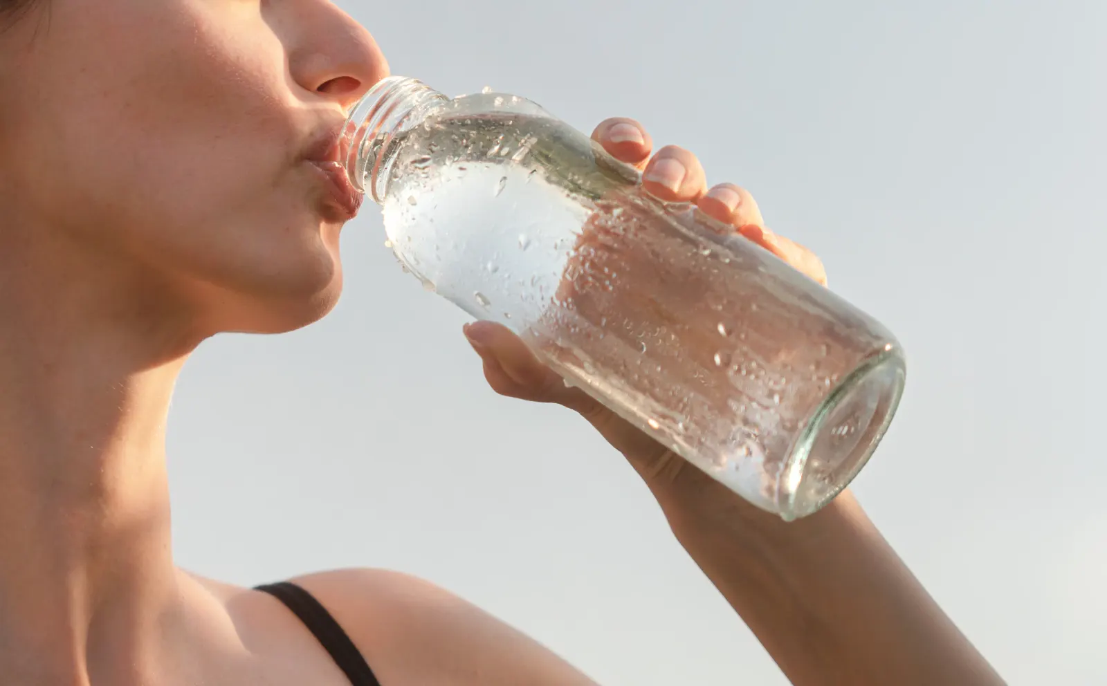 Close-up of a woman drinking from a glass water bottle to stay hydrated and replenish fluids