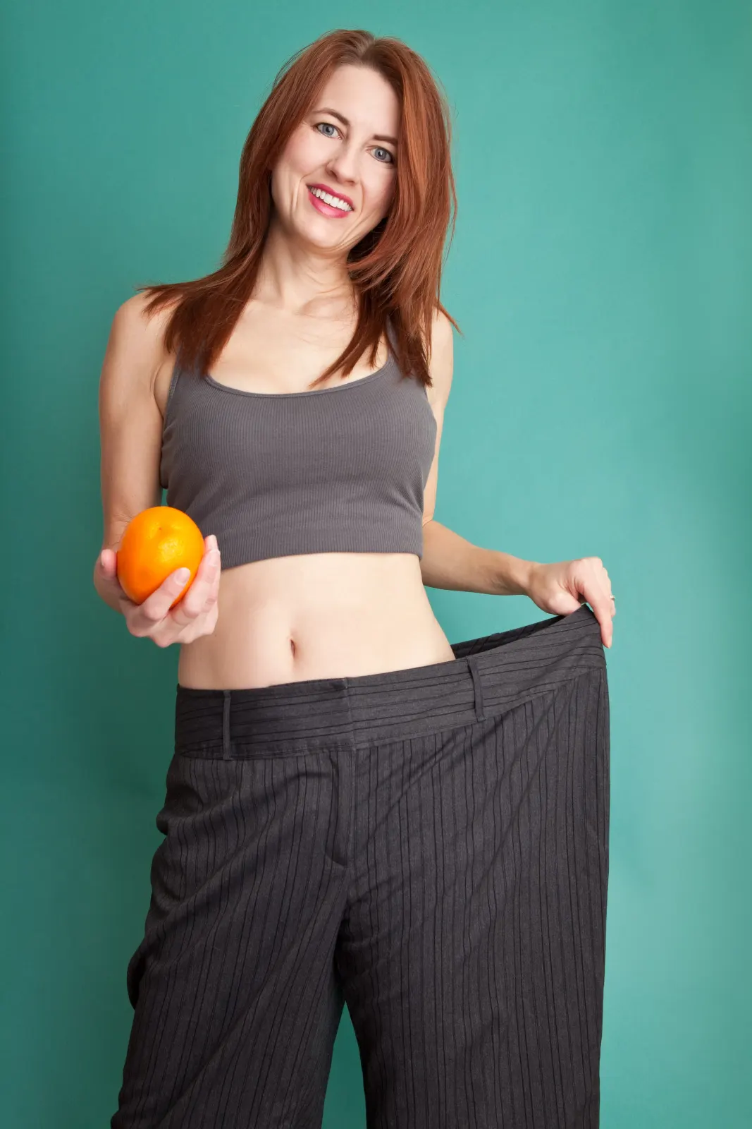 Woman holding an orange and pulling out oversized pants after lipotropic weight loss support
