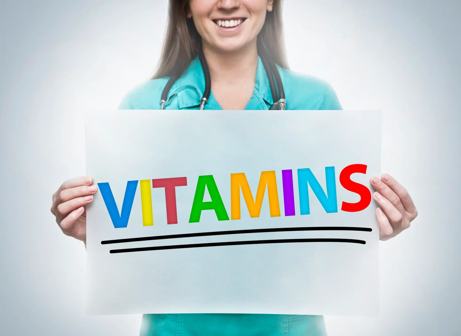Smiling clinician in scrubs holding a colorful VITAMINS sign for radiant wellness IV therapy