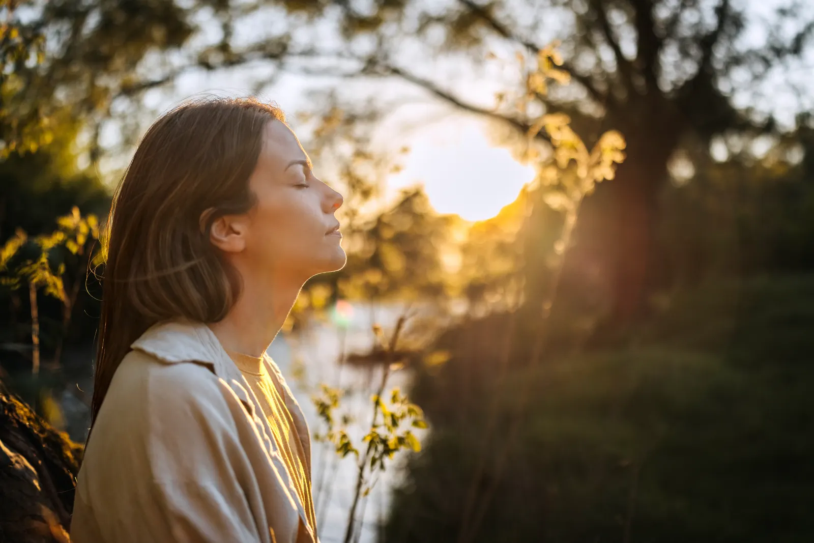 Woman with eyes closed soaking in golden sunset light, glowing and radiant outdoors