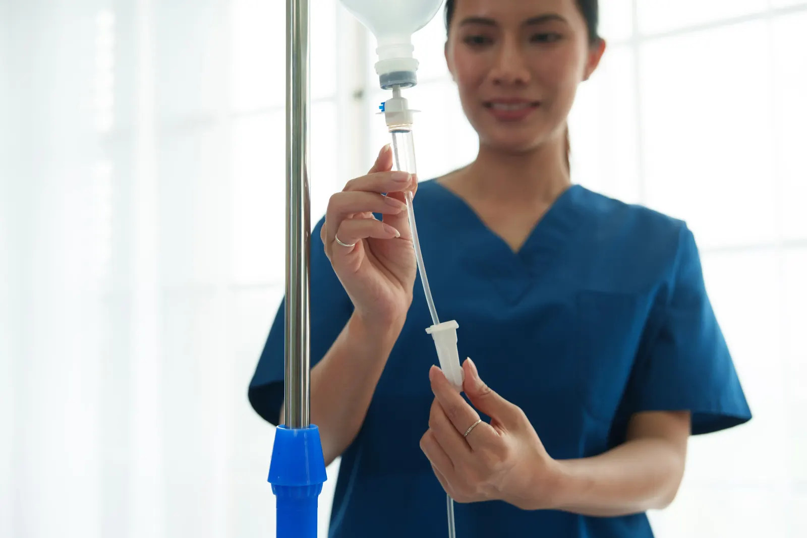 Clinic staff member in blue scrubs priming an IV line and bag for NAD infusion treatment