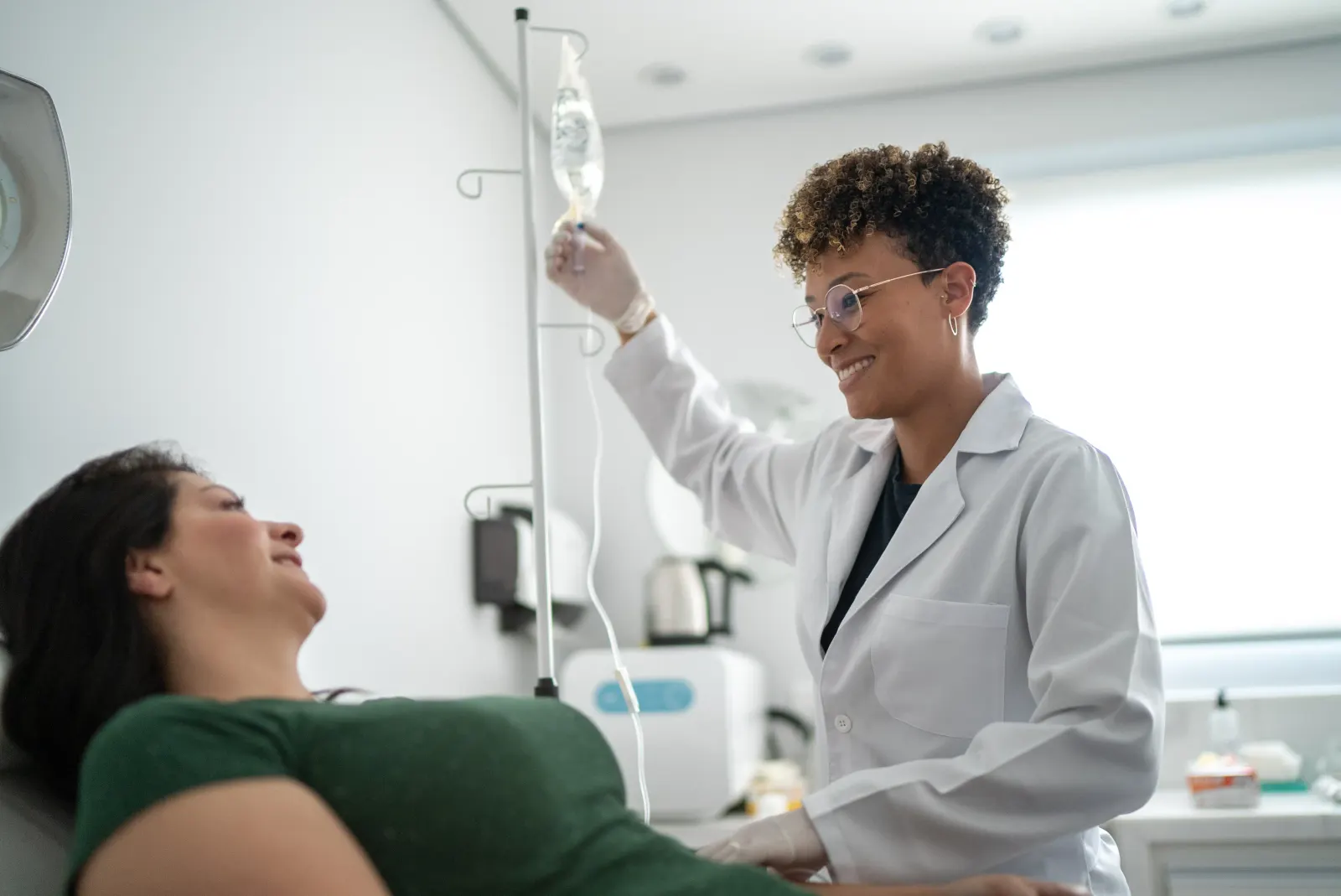 Smiling clinician adjusting an IV line for a reclining patient during NAD therapy in New Rochelle