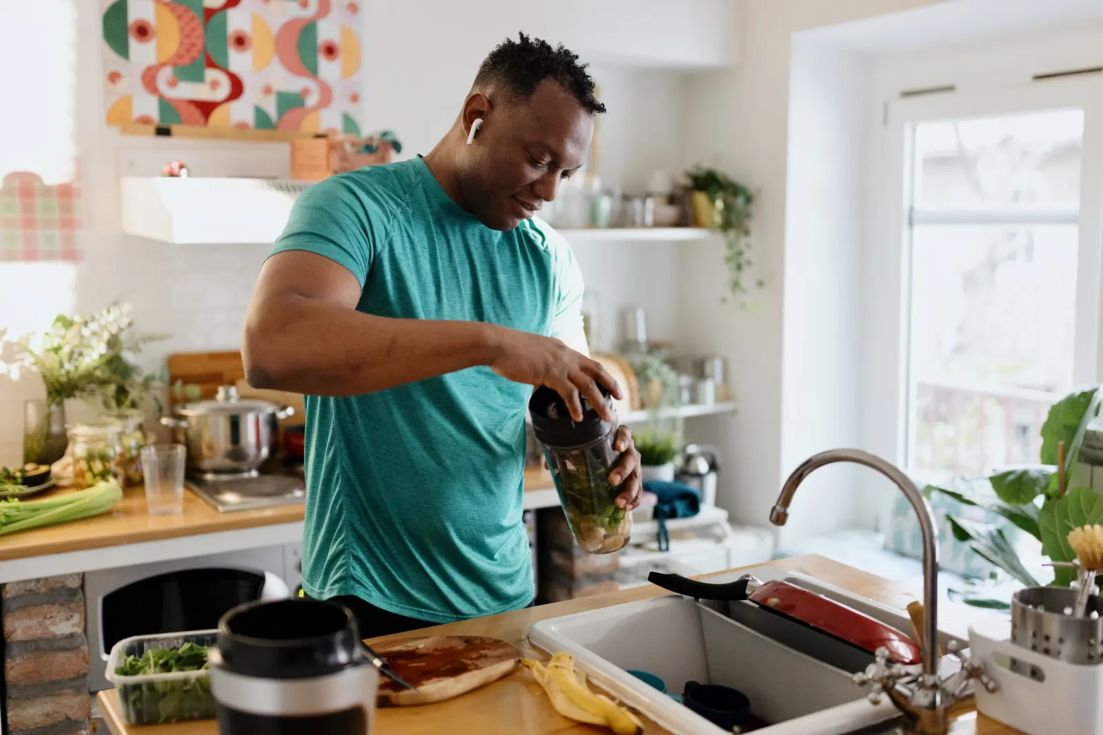 Athletic man blending a green smoothie in a bright kitchen, supporting performance and nutrition