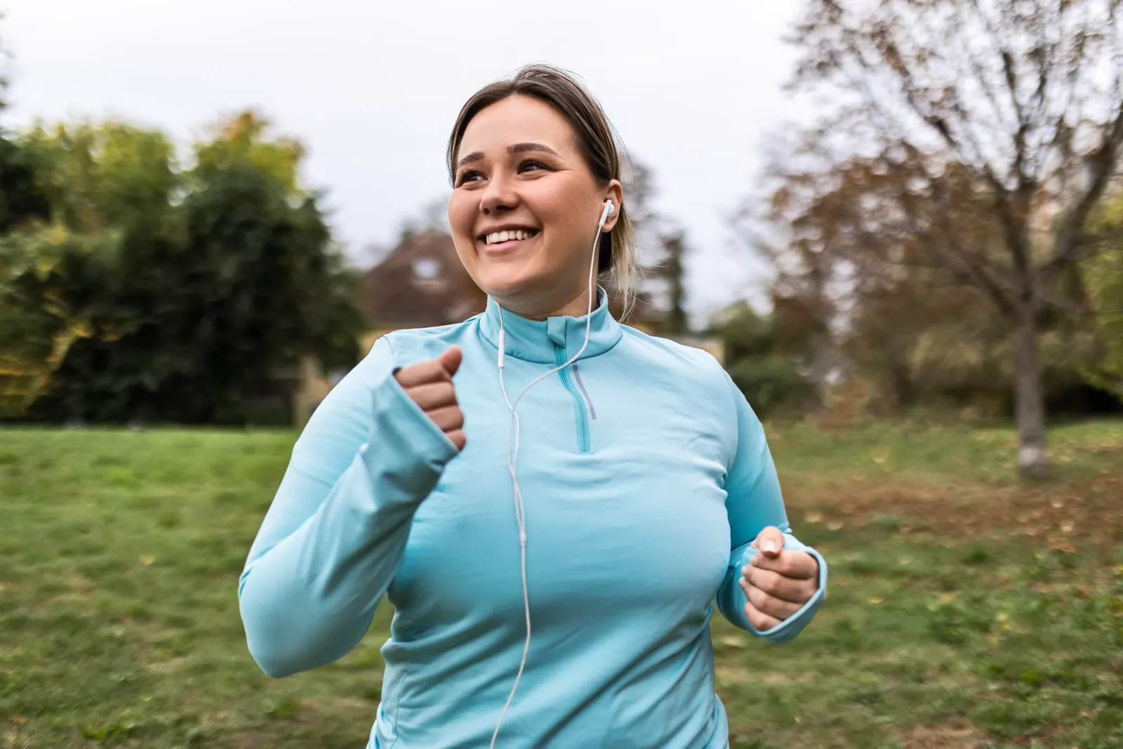 Smiling woman jogging outdoors in a park, reflecting fitness and performance wellness goals
