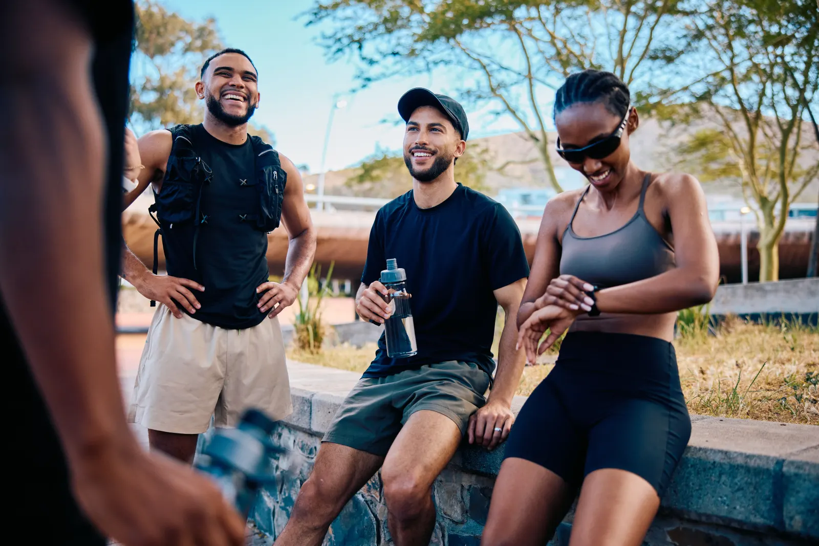 Three active friends laughing and hydrating outdoors after a workout, staying well together